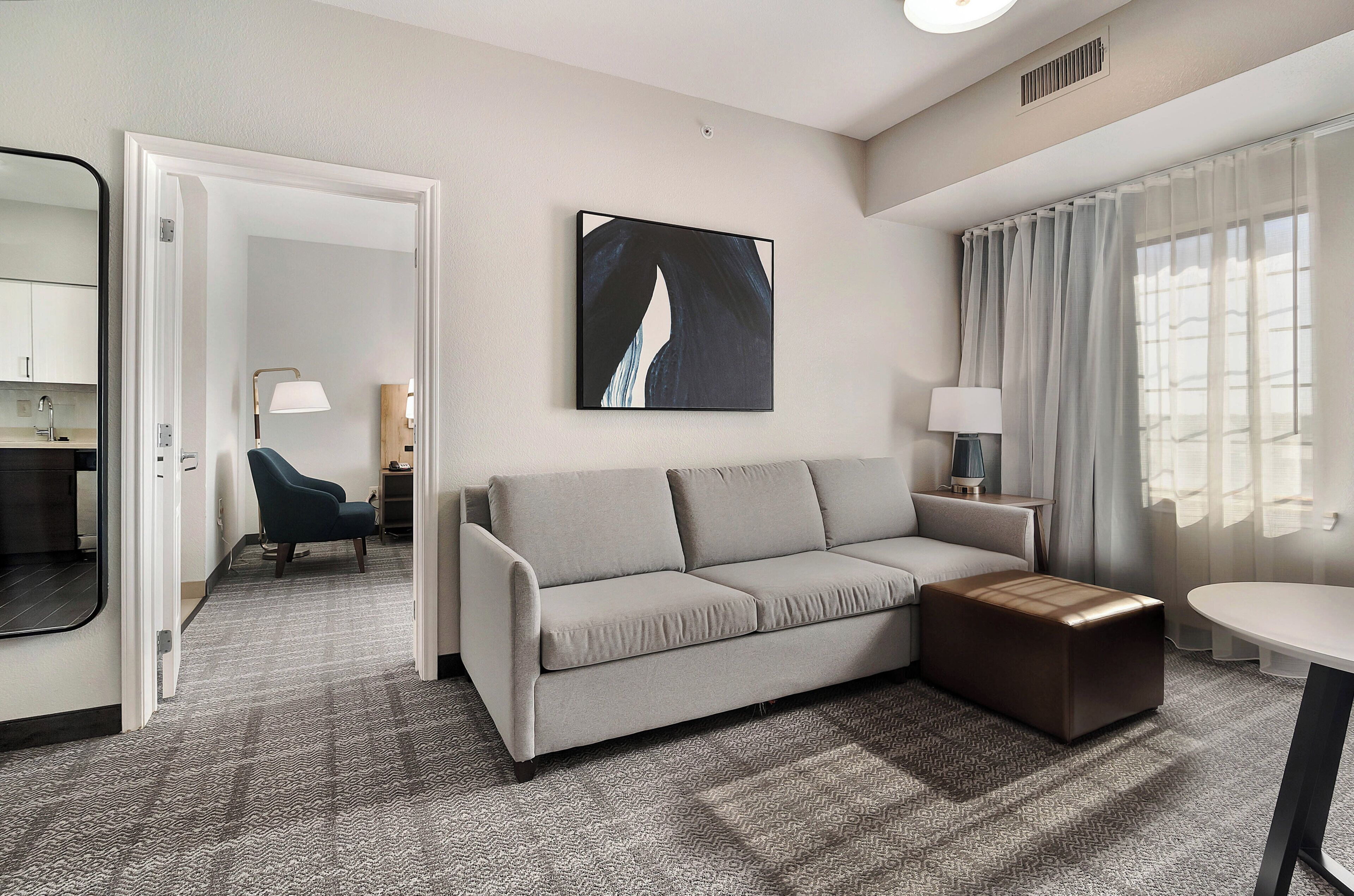 Une chambre d’hôtel moderne, dotée d’un canapé, d’un pouf et d’un tableau au mur.
