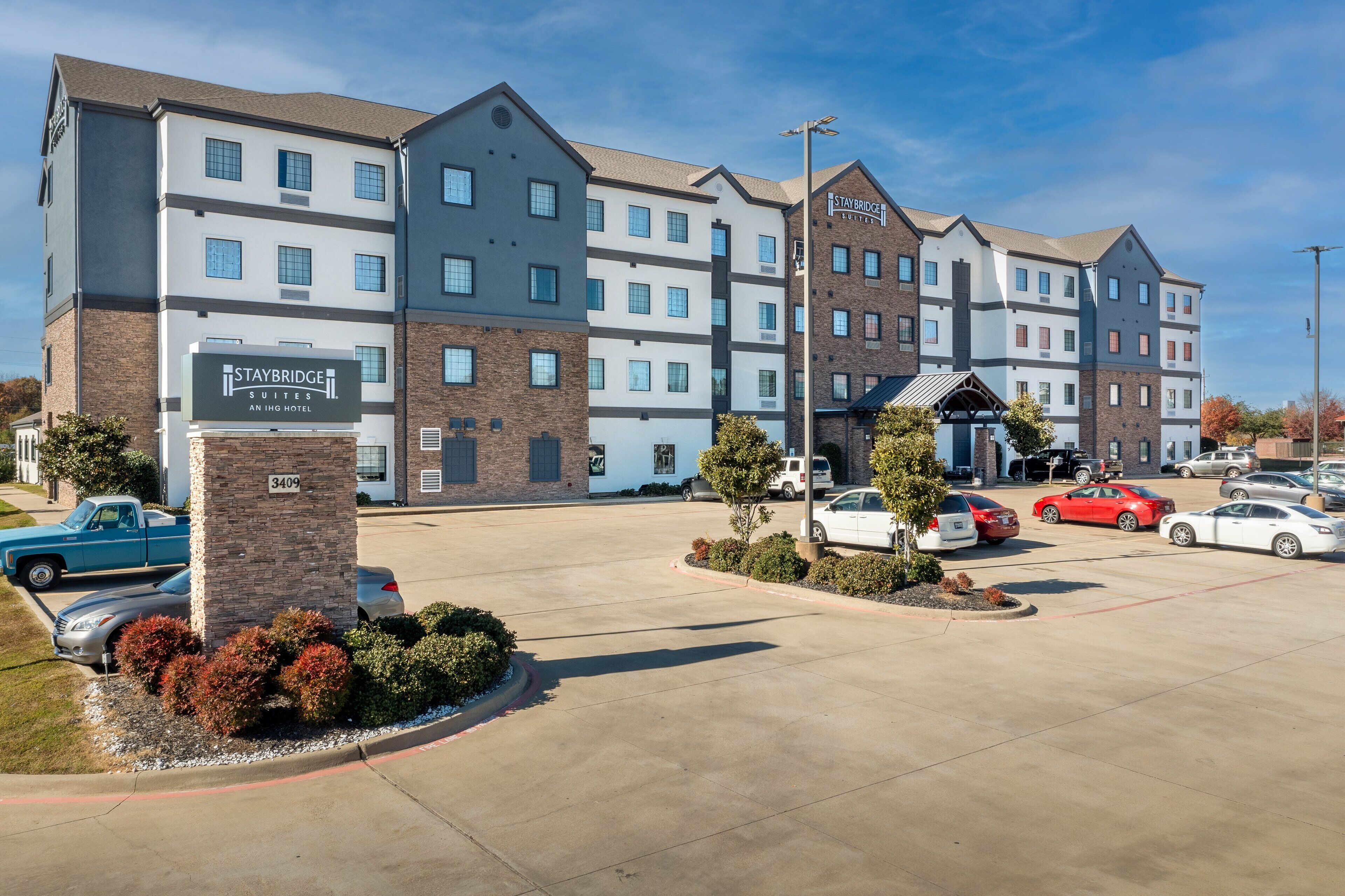 A Staybridge Inn hotel with a parking lot, multiple cars, and a clear sky.