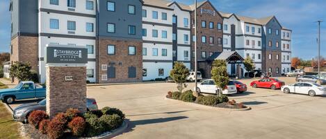 A Staybridge Inn hotel with a parking lot, multiple cars, and a clear sky.
