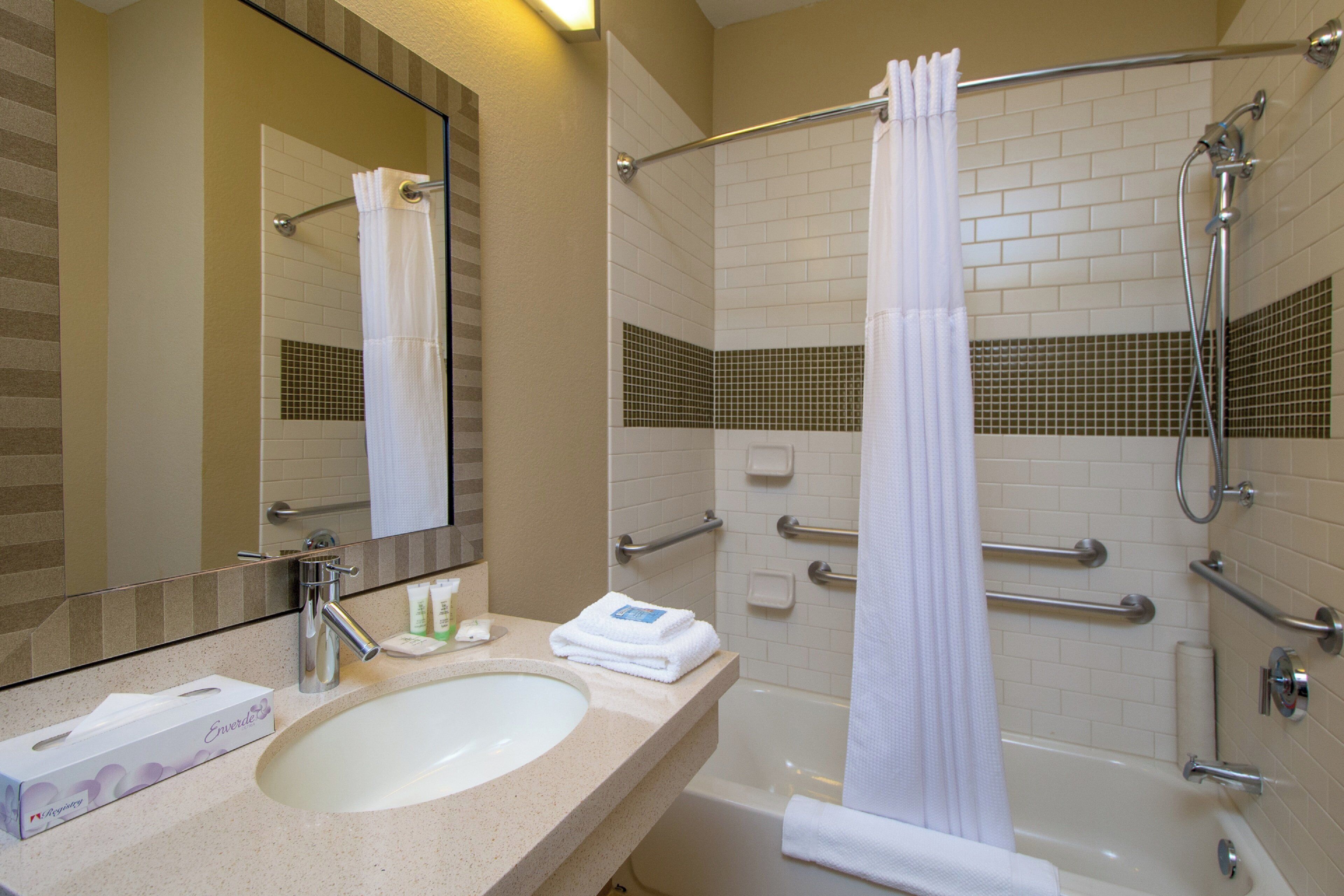 A bathroom with a sink, mirror, and shower area.