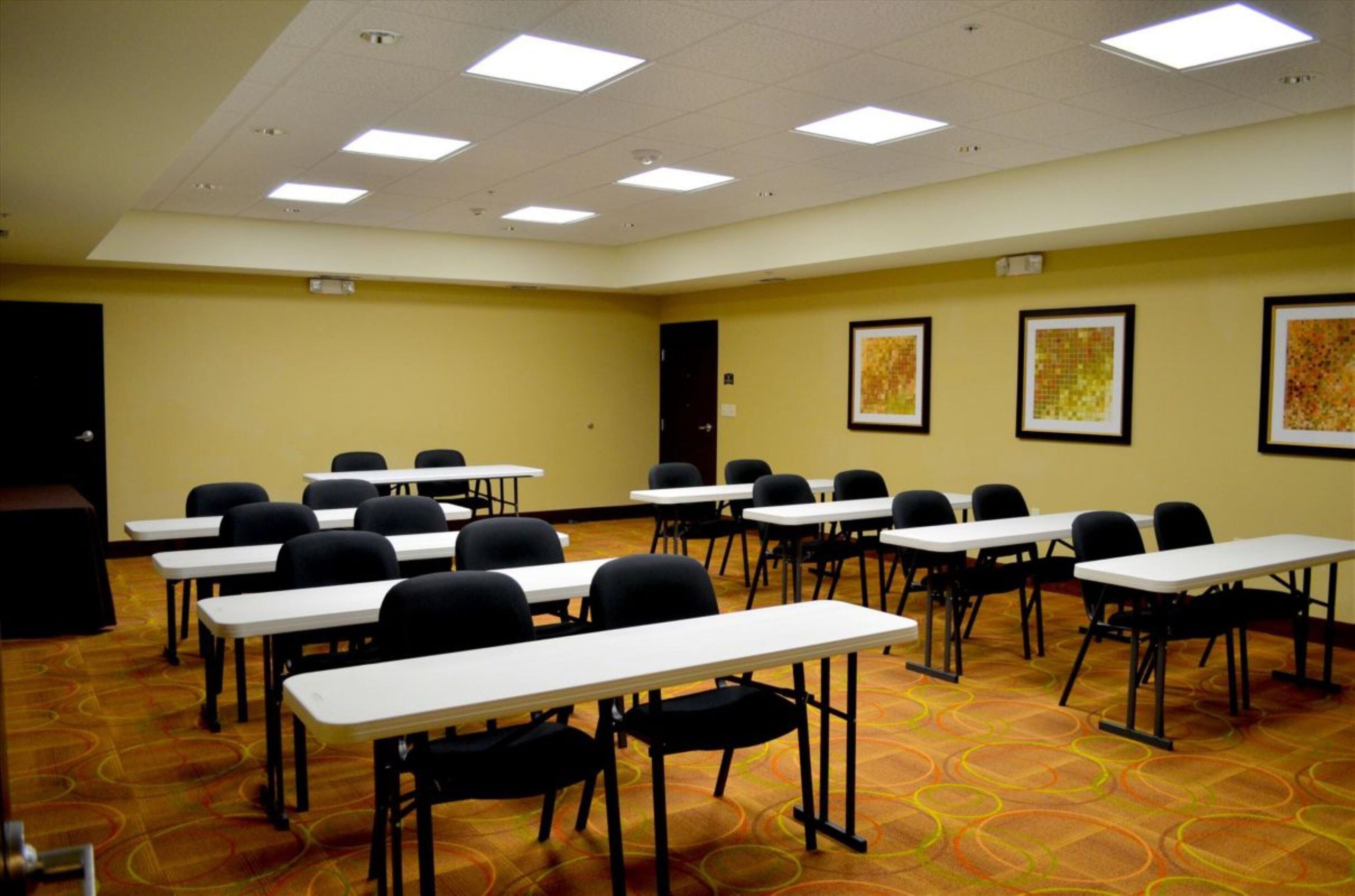 A conference room with multiple tables and chairs, a carpeted floor, and ceiling lights.