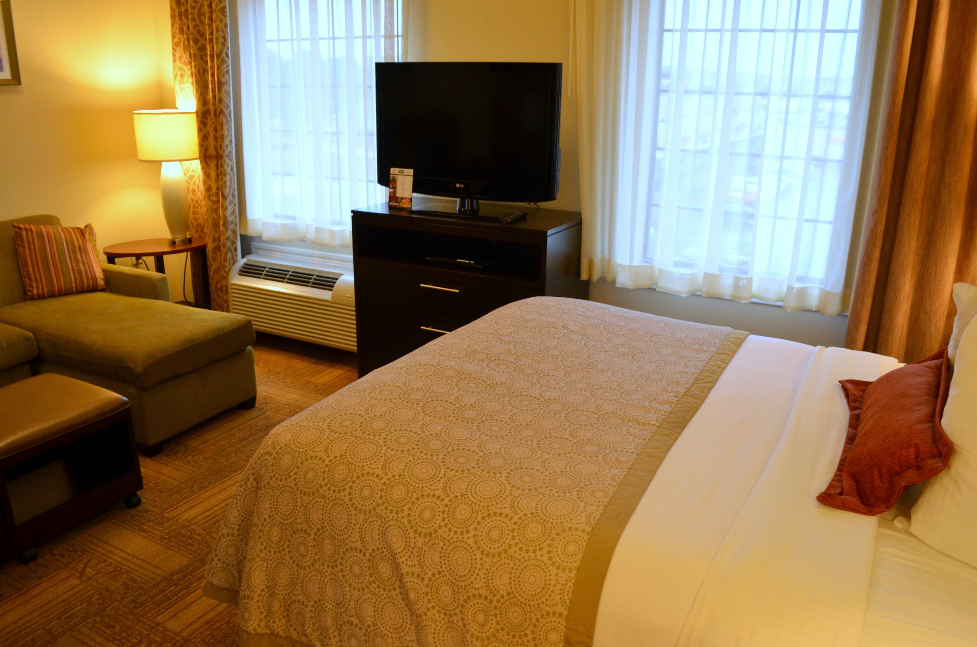 A hotel room with a bed, a television on a dresser, a sofa, and a window with curtains.