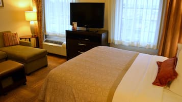 A hotel room with a bed, a television on a dresser, a sofa, and a window with curtains.