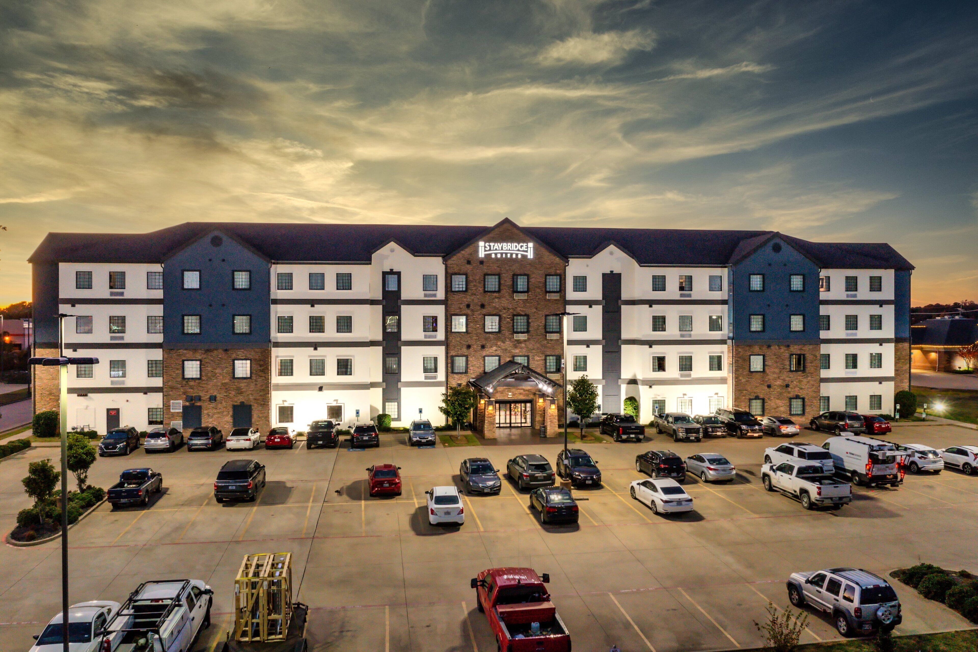 A multi-story hotel with a central entrance, parking lot, and a sign reading "STAYBRIDGE".