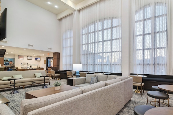 Un hall d’hôtel spacieux, doté d’un grand canapé d’angle, d’une table basse et d’un coin repas avec une table ronde et des chaises.
