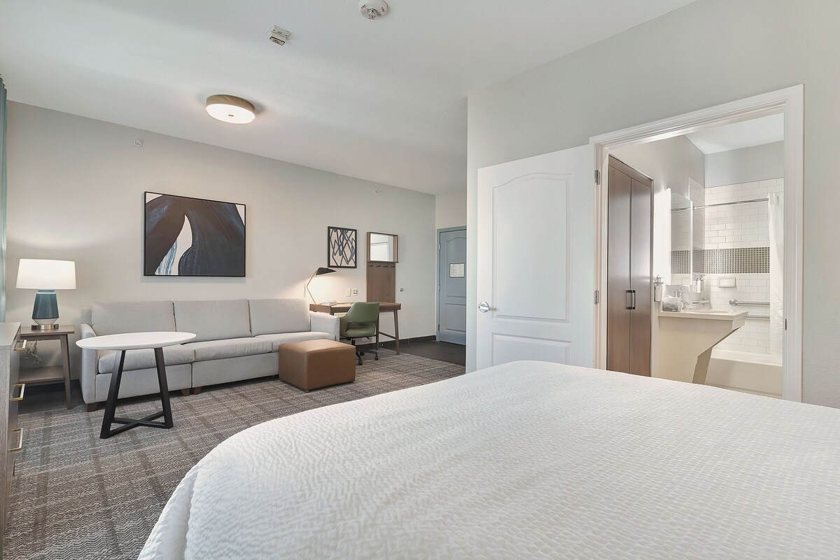 Et hotelværelse med en stor seng, en sofa, et skrivebord og et badeværelse, der kan ses igennem en åben dør.