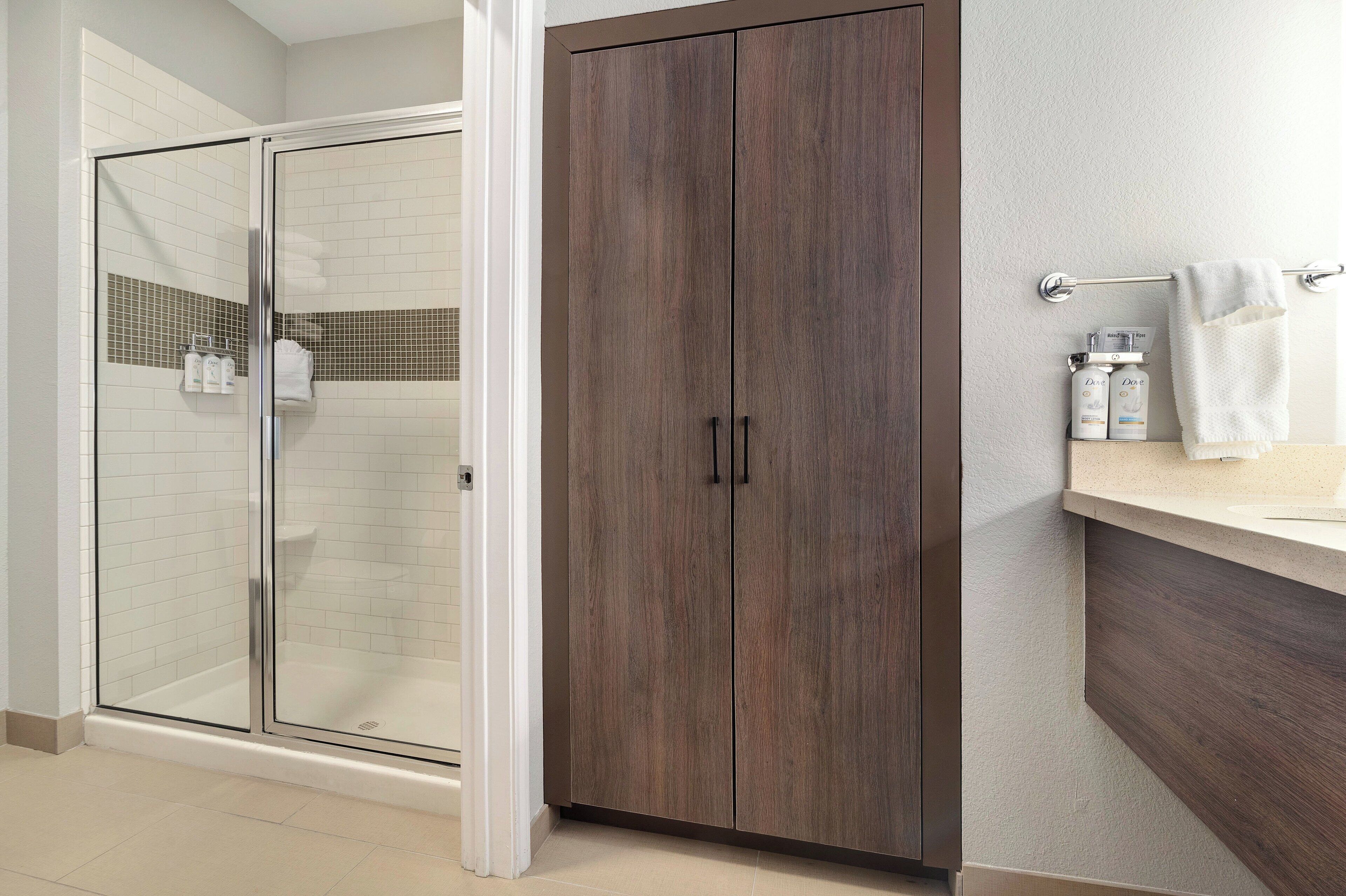 A bathroom with a glass shower enclosure, a wooden wardrobe, and a countertop with toiletries.