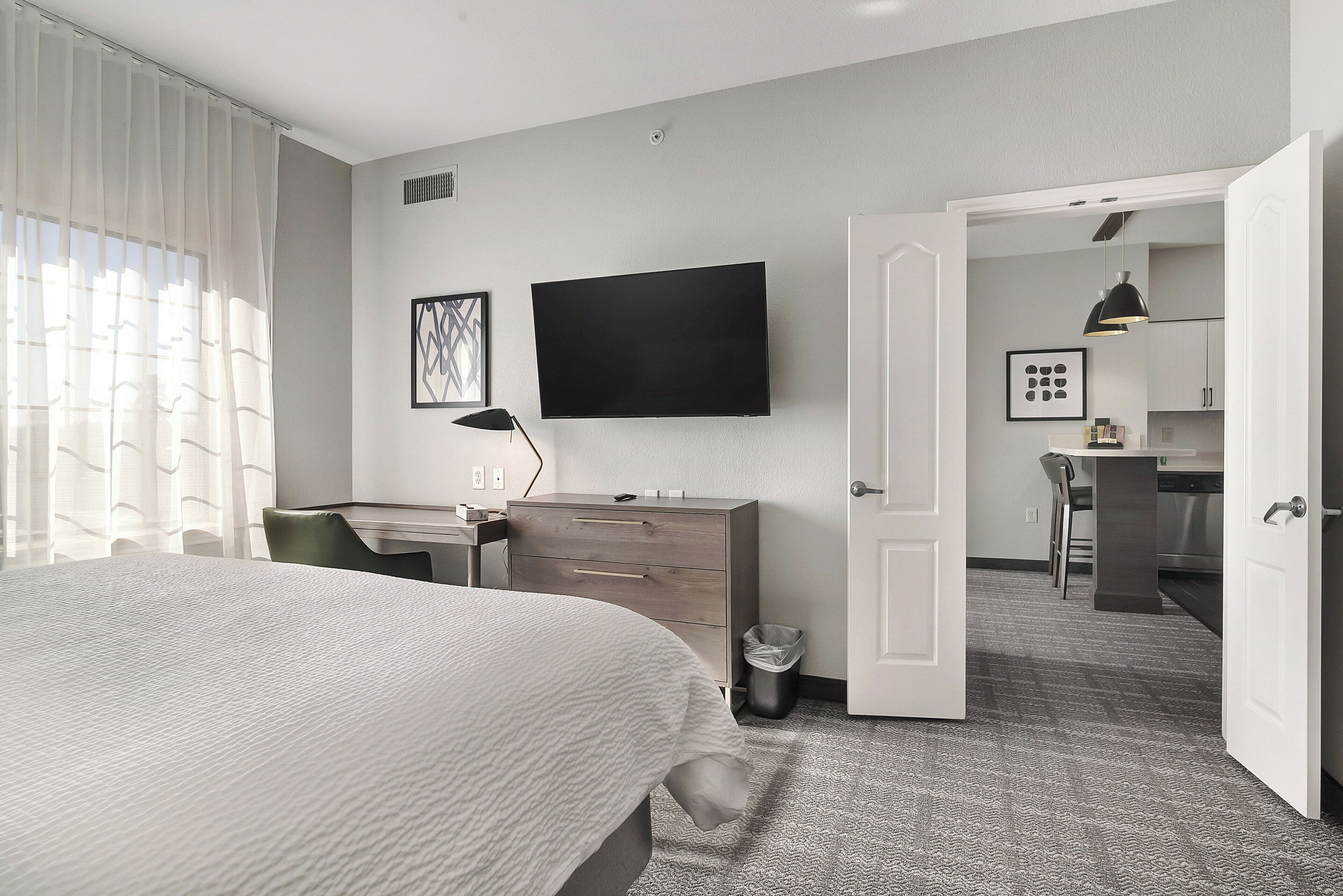 Una habitación de hotel con cama, escritorio, televisor y puerta que da a una kitchenette.