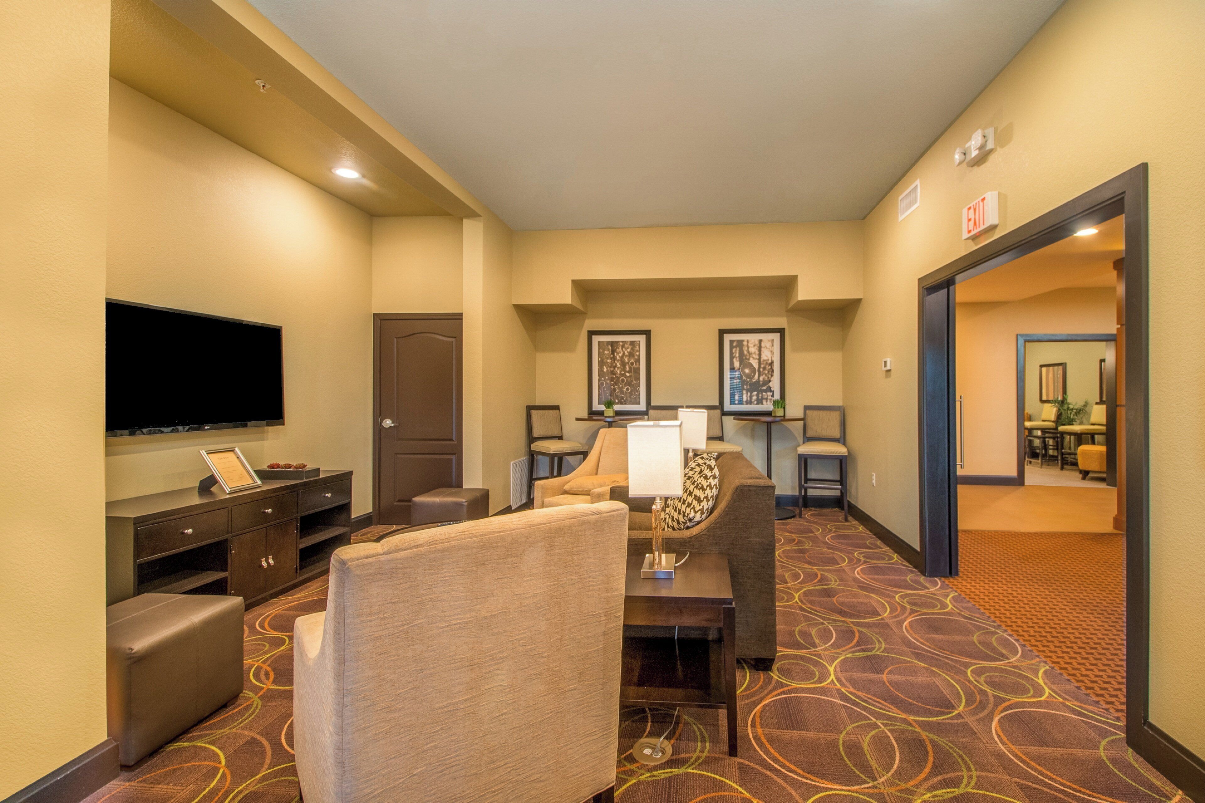 A hotel lobby with a flat-screen TV, a seating area with a table and chairs, and framed artwork on the walls.