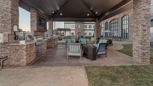 Un patio exterior con pilares de piedra, una parrilla y asientos.