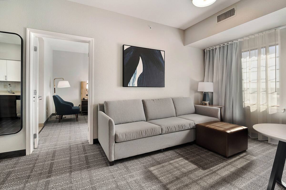 A modern hotel room with a sofa, ottoman, and a painting on the wall.