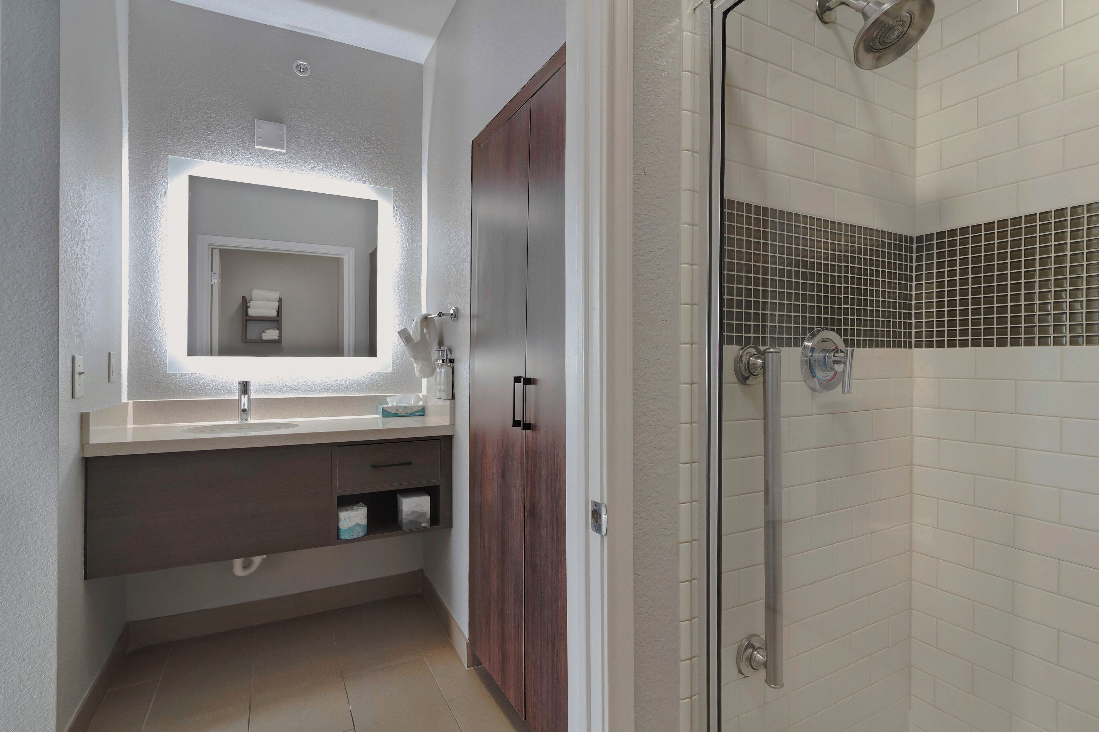 A modern bathroom with a vanity, mirror, and shower area.