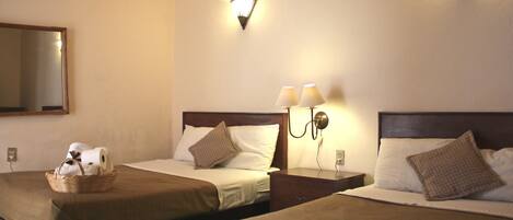 Une chambre d’hôtel avec deux lits, chacun doté d’une tête de lit, d’une table de chevet et d’une lampe. On trouve un panier avec des serviettes sur le lit situé à gauche.