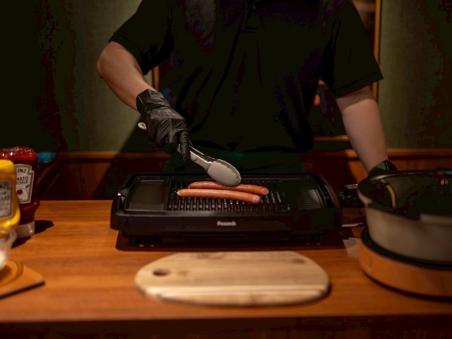 A person grilling sausages on a portable grill.