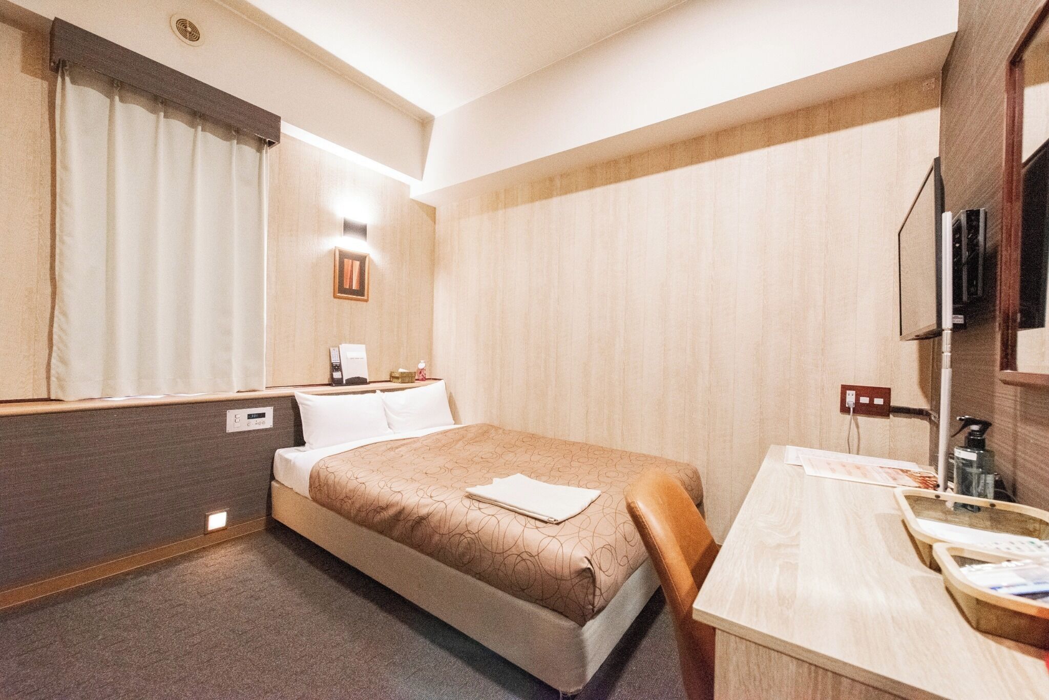 Ein Hotelzimmer mit einem Bett, einem Schreibtisch mit Stuhl, einem Spiegel und einem Fernseher.