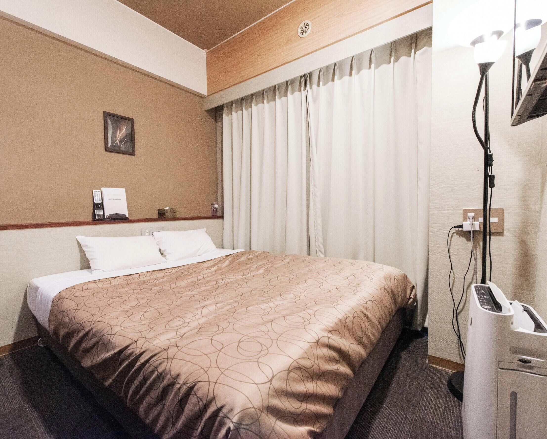 Habitación de hotel con cama, escritorio, teléfono y lámpara.