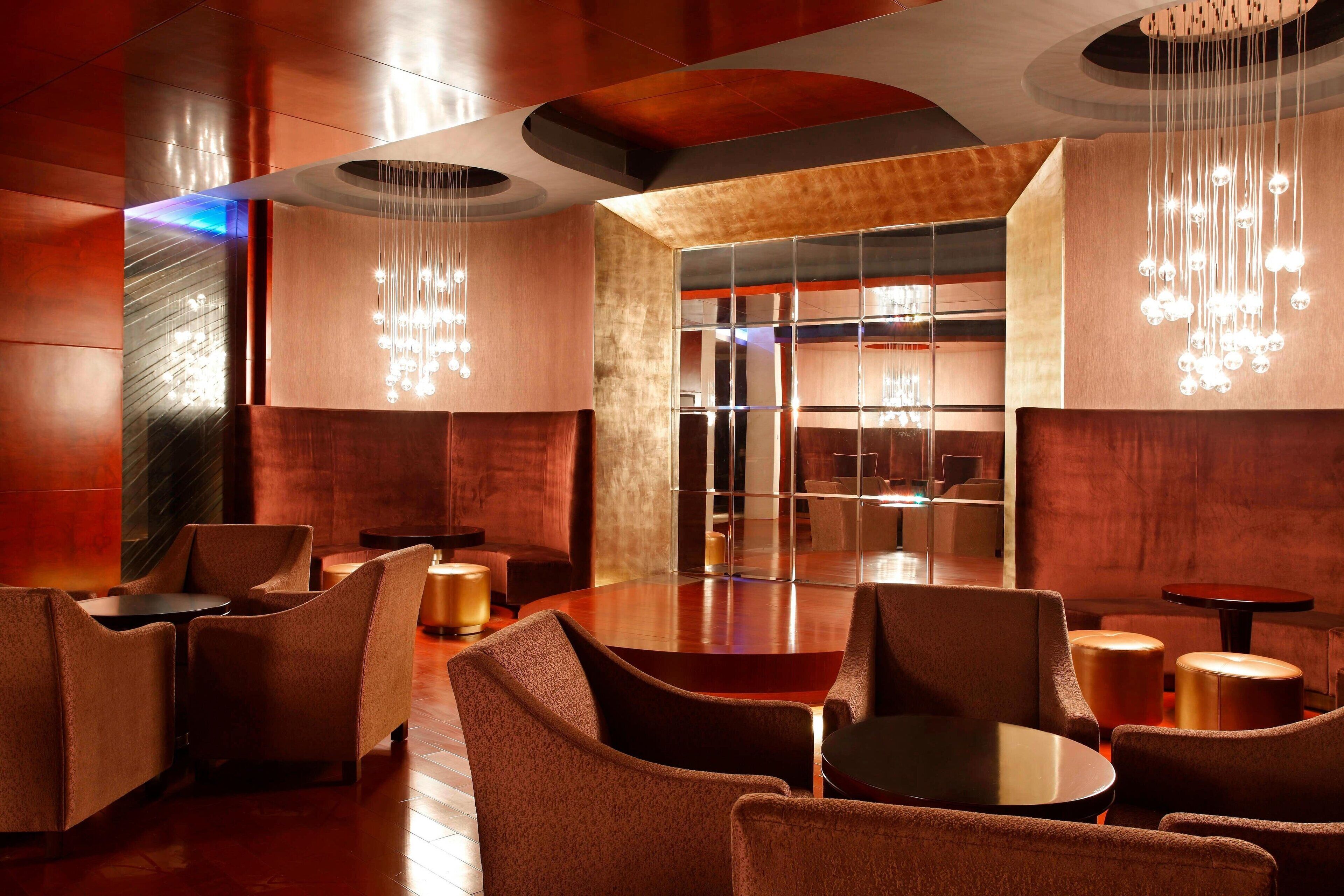 A modern lounge area with leather sofas, a round table, and hanging light fixtures.