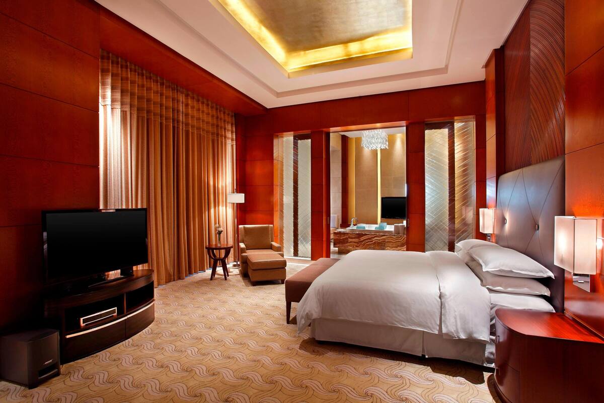 Une chambre d’hôtel dotée d’un grand lit, d’une télévision, d’un coin salon et d’une salle de bain avec un grand miroir.