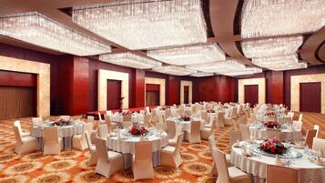 A banquet hall with round tables set for events, featuring a patterned carpet and chandeliers.