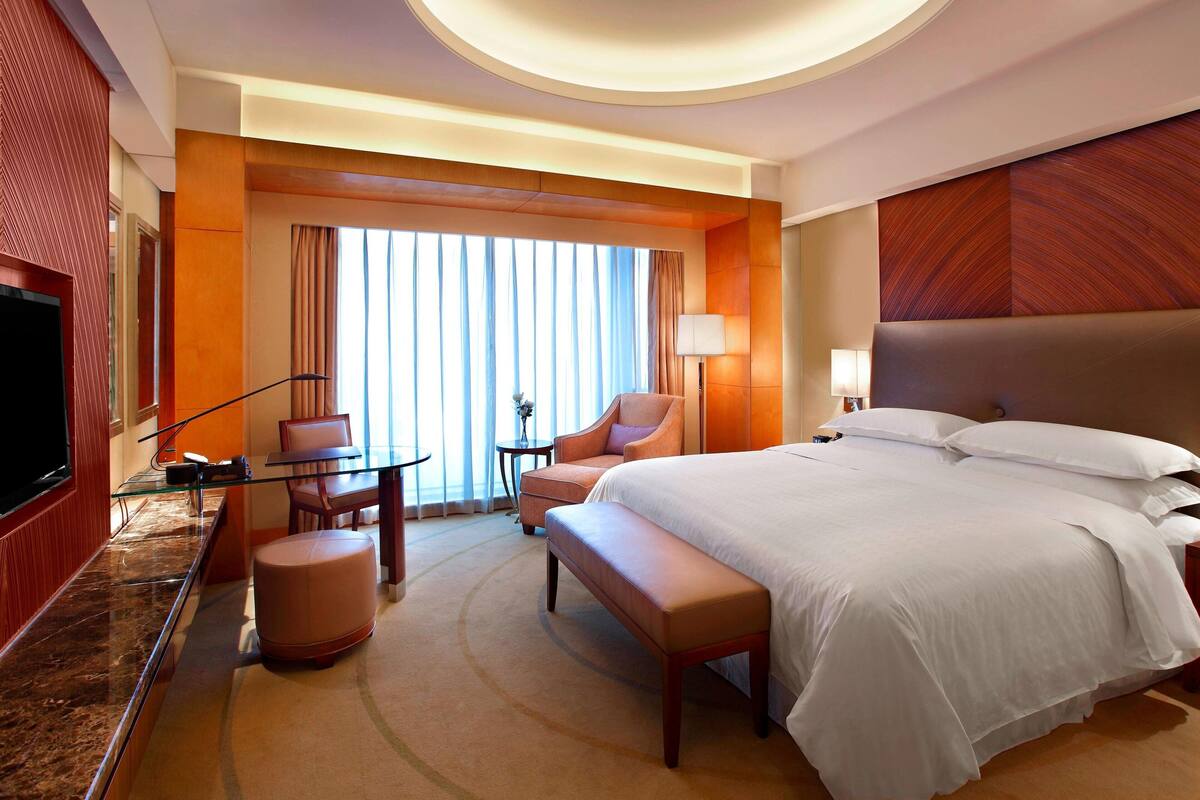 Une chambre d’hôtel avec un grand lit, une télévision, un bureau avec une chaise et une petite table avec une lampe.