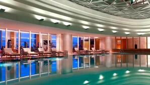 Piscina interior moderna con sillones de descanso y un techo alto con diseños geométricos.