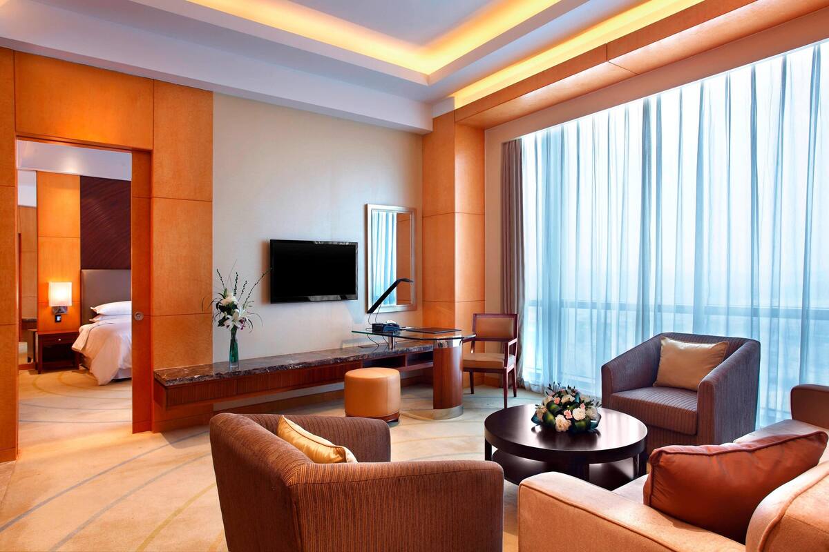 Une chambre d’hôtel moderne dotée d’une grande fenêtre, d’un téléviseur à écran plat, d’un canapé, d’une table basse et d’un bureau avec une lampe.