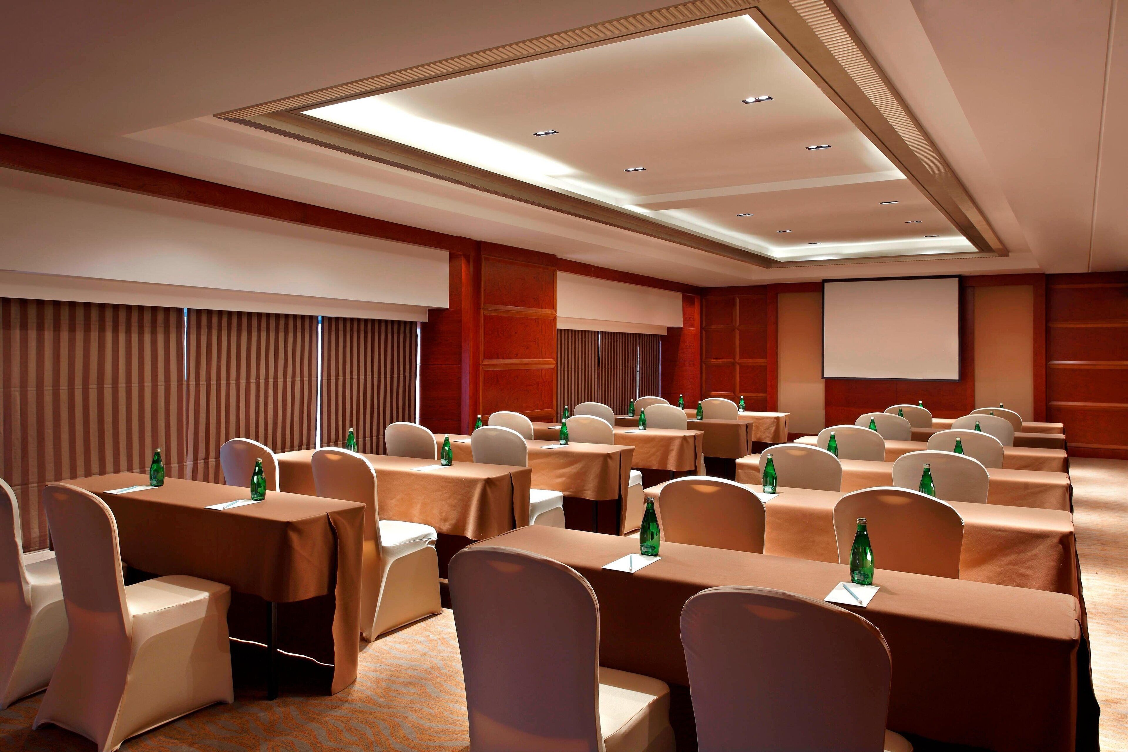 A conference room with multiple tables, chairs, and a projector screen.
