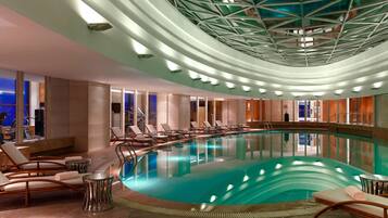Relax by the oval-shaped pool surrounded by lounge chairs and tables, set amidst a spacious and well-lit area.