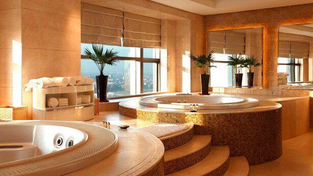 Un baño lujoso con dos tinas grandes, una zona de estar con toallas y vistas a la ciudad.