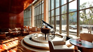 Un vestíbulo amplio con un piano de cola, asientos cómodos y grandes ventanales que ofrecen vistas de la ciudad.