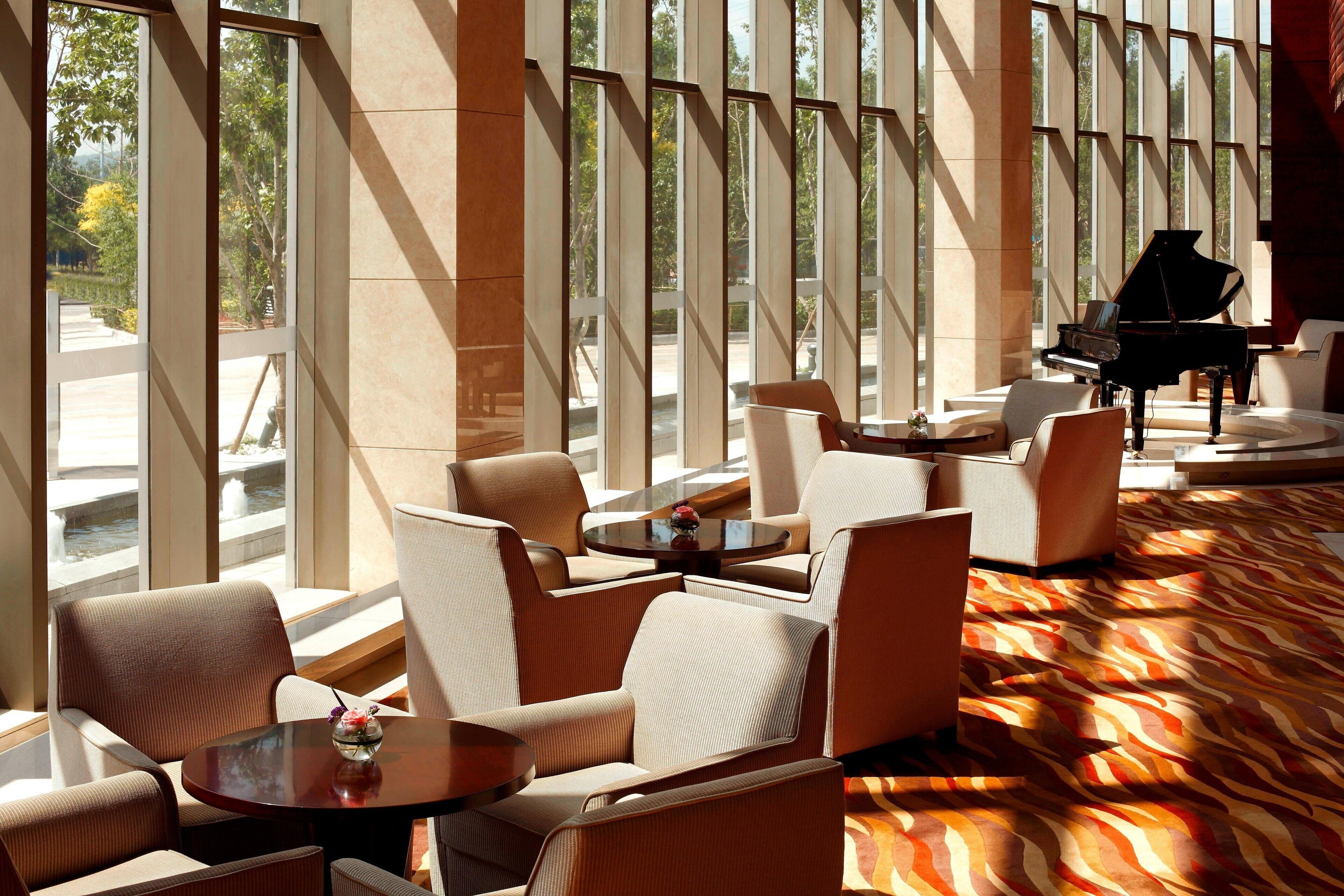 A spacious lobby with large windows, a grand piano, and comfortable seating areas.