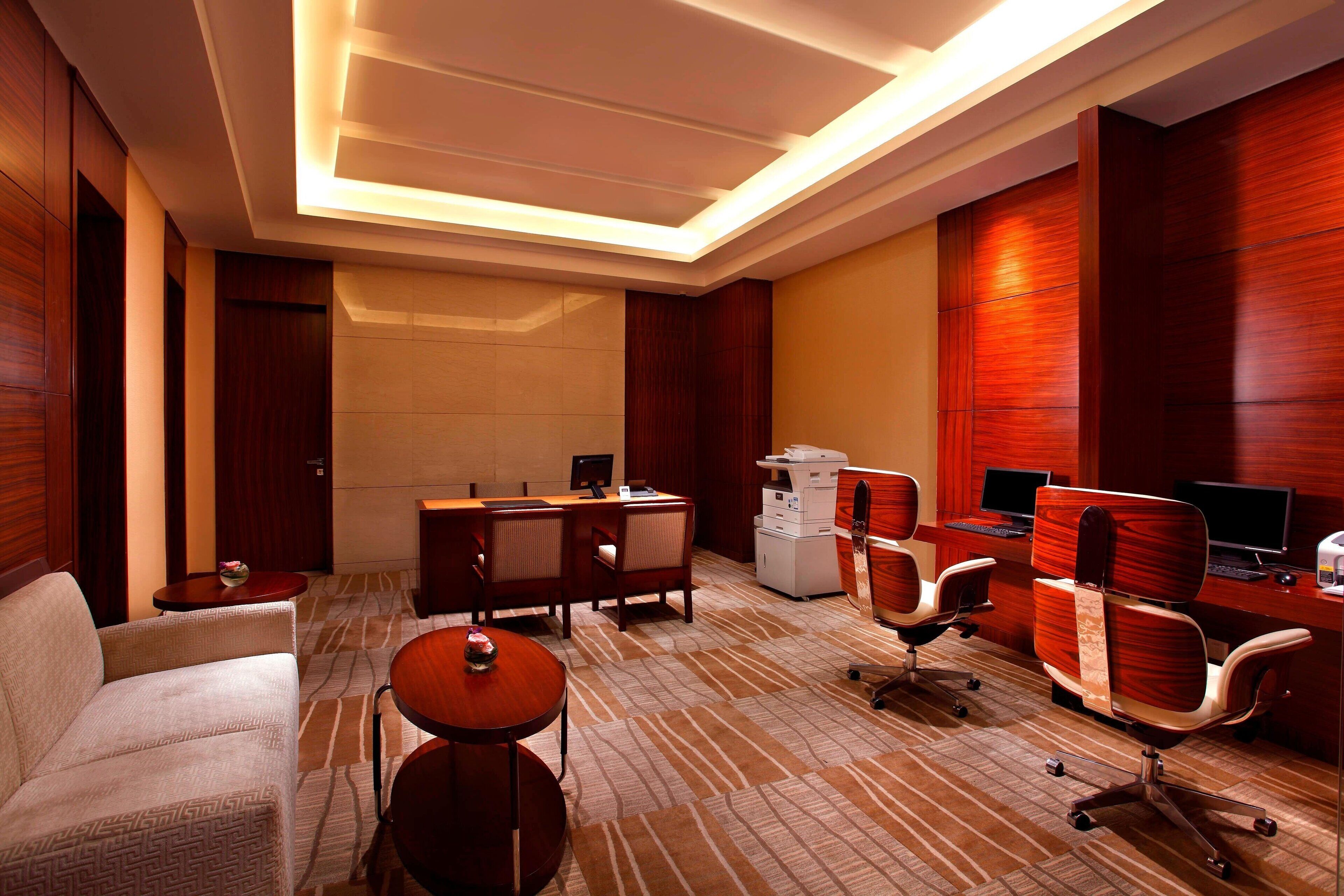 A hotel room with a sofa, a dining table, a desk with a computer, and a TV.