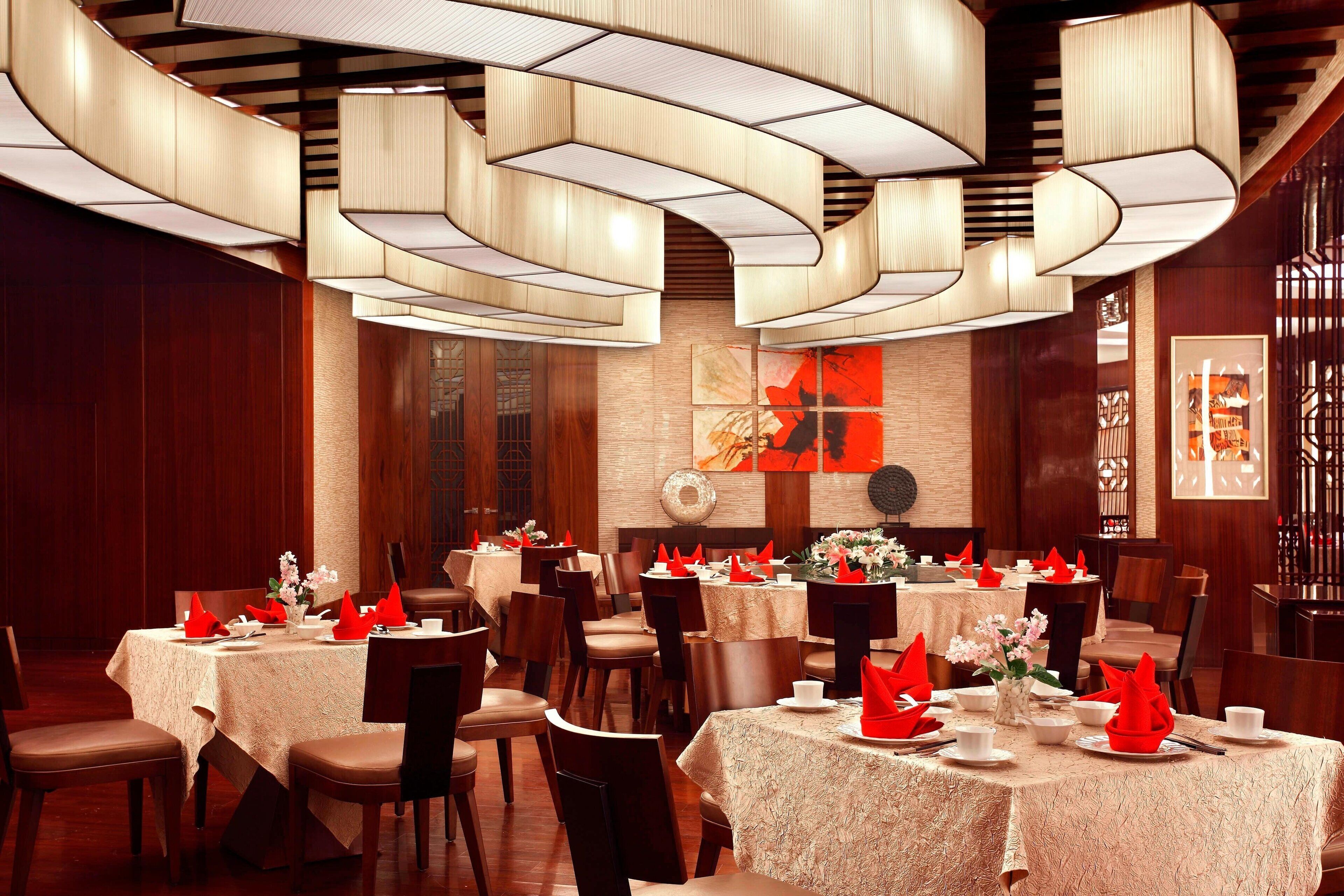 A restaurant with round tables, red napkins, and modern lighting fixtures.