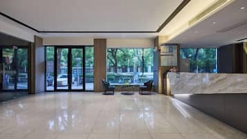 A spacious lobby with a reception desk, seating area, and large windows offering a view of the outdoors.