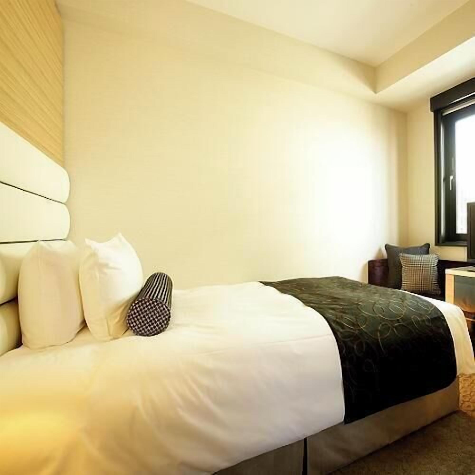 Une chambre d’hôtel avec un lit, des oreillers, une table de chevet et une fenêtre.