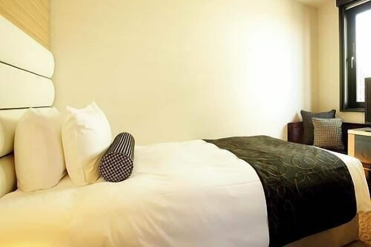 Une chambre d’hôtel avec un lit, des oreillers, une table de chevet et une fenêtre.