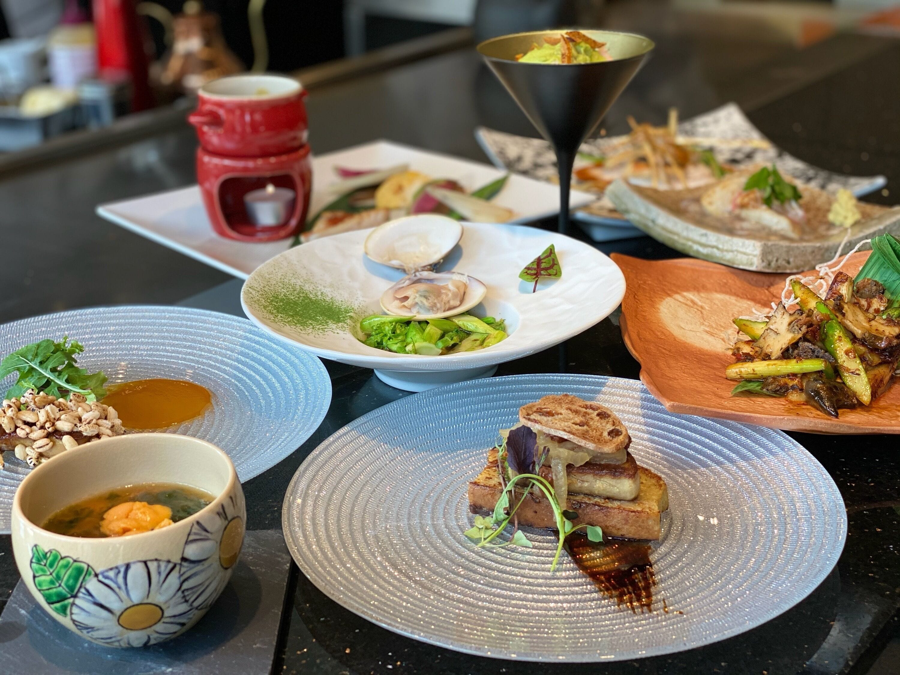 Variedad de platillos en una mesa, incluyendo un tazón de sopa, un plato con ensalada verde y un plato con carne a la parrilla.