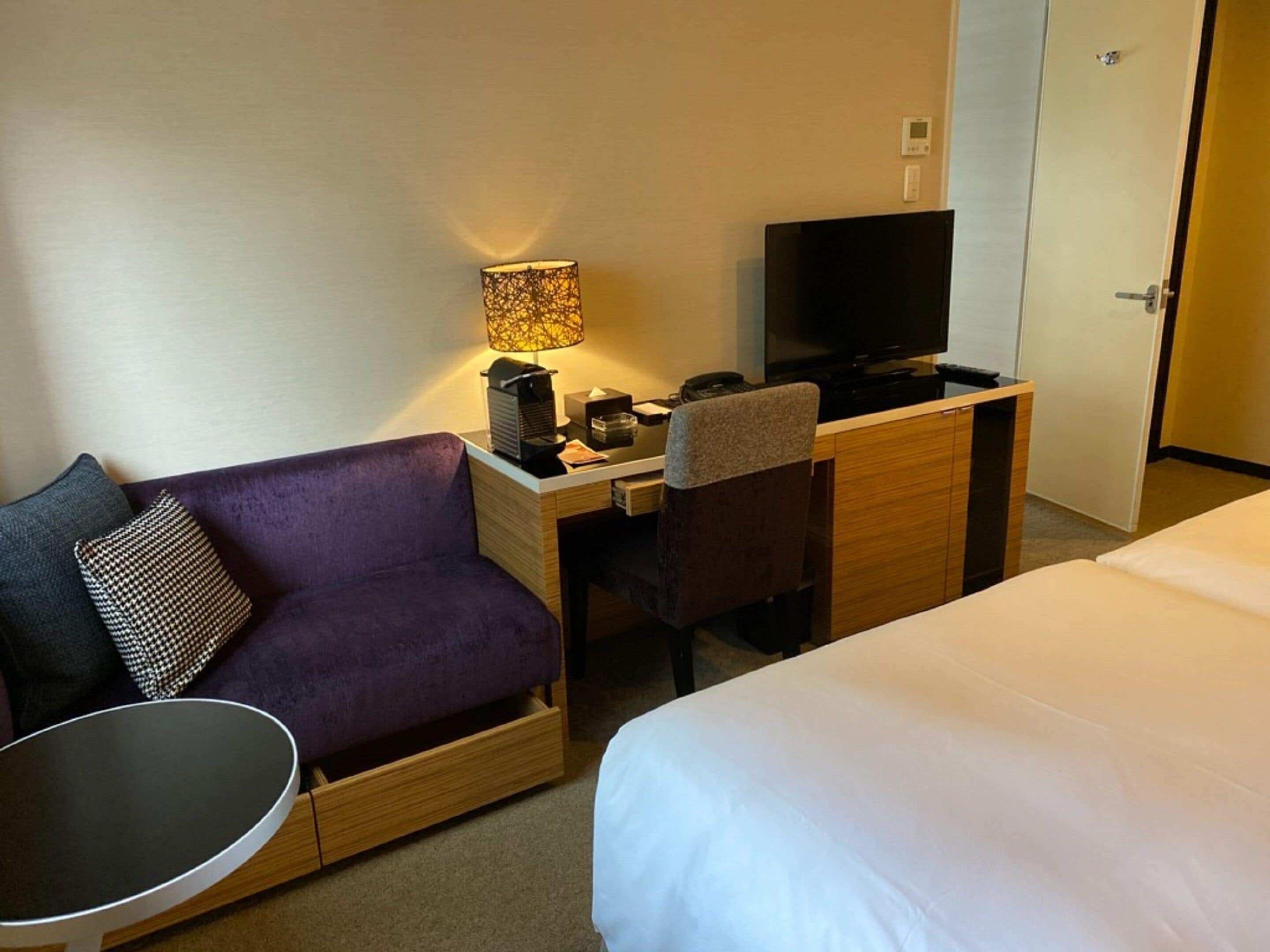 A hotel room with a sofa, a desk with a computer, a TV, and a bed.