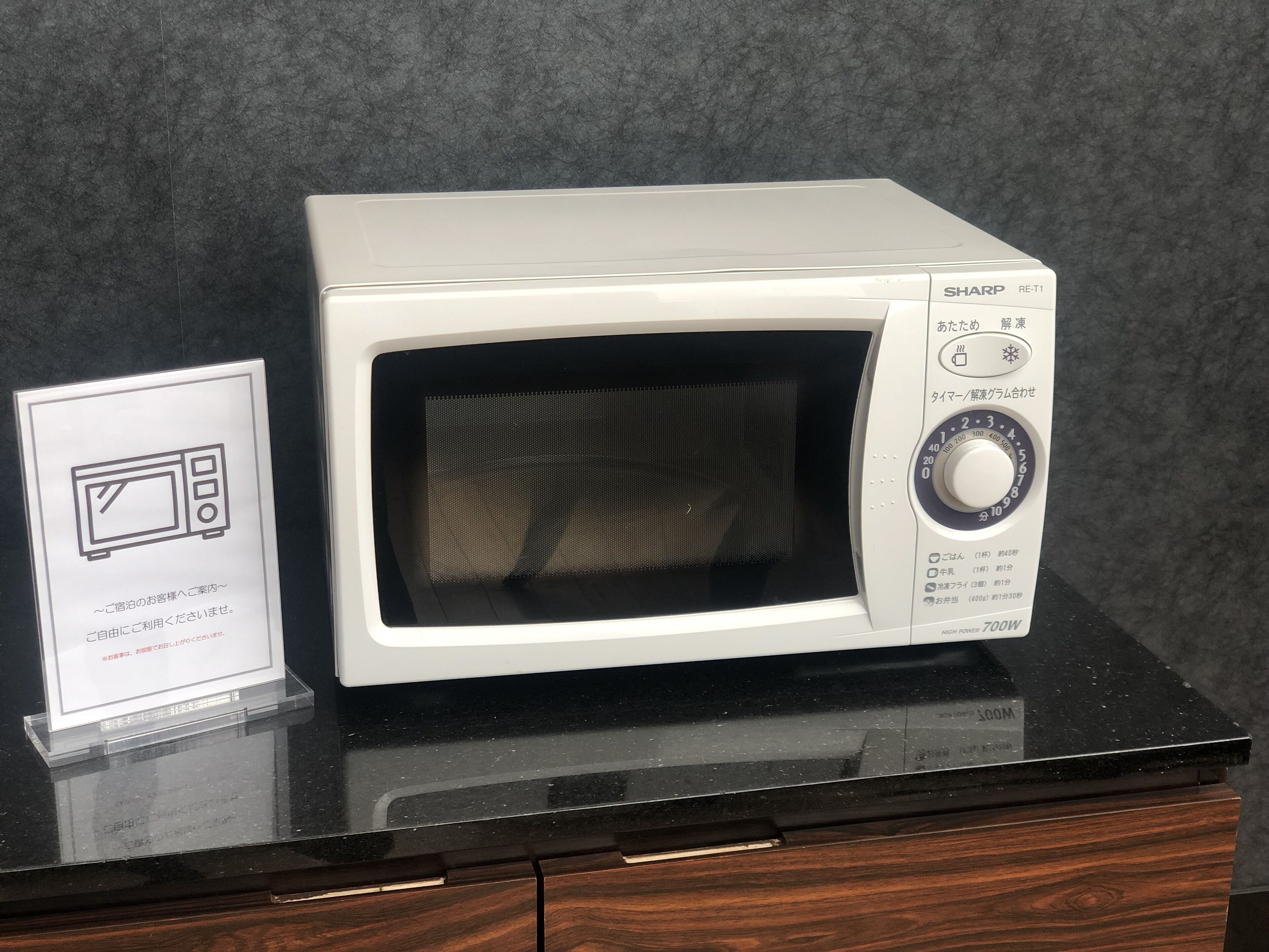 A white Sharp microwave oven with a digital display and a power button on a black countertop.