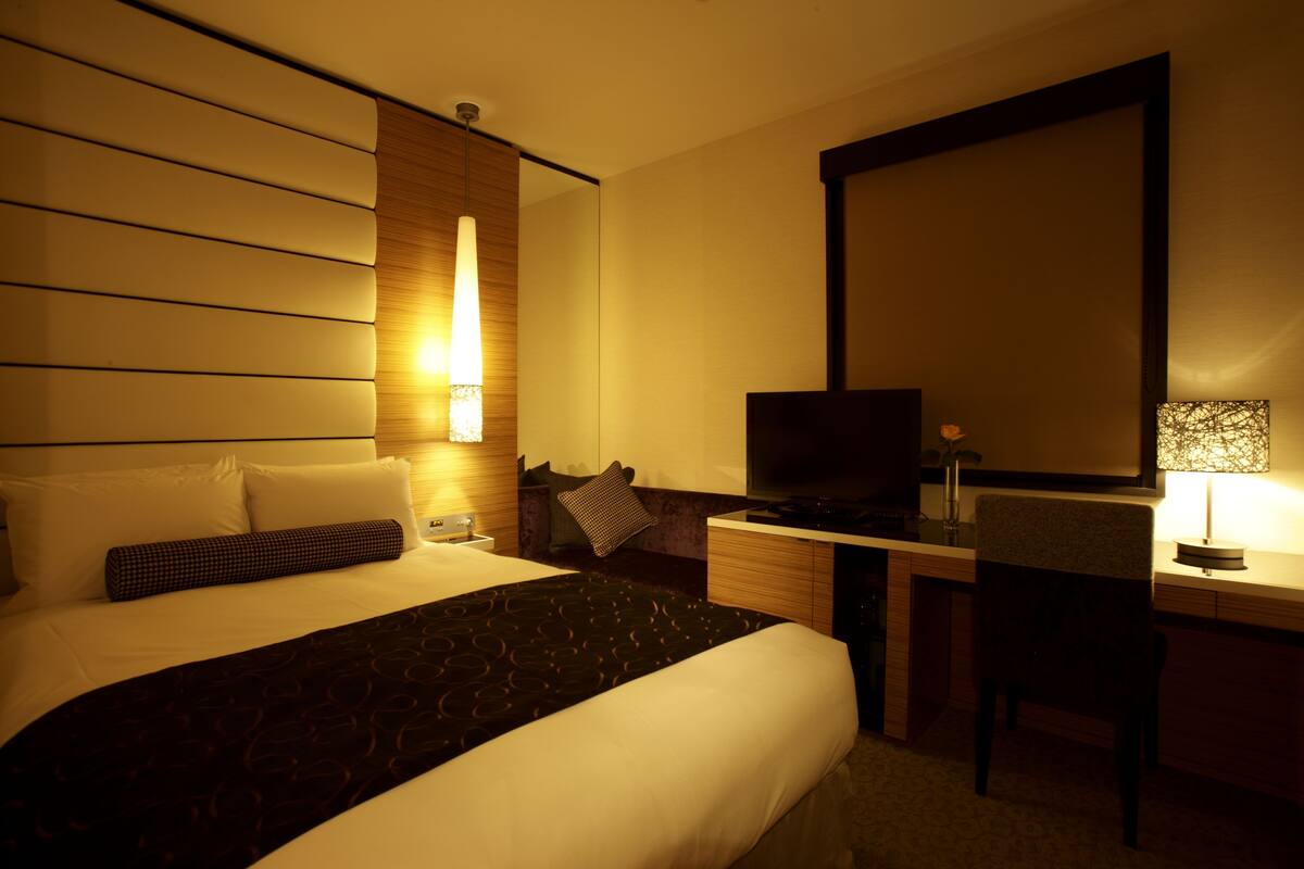 Une chambre d’hôtel avec un grand lit, un bureau avec une télévision et une chaise.