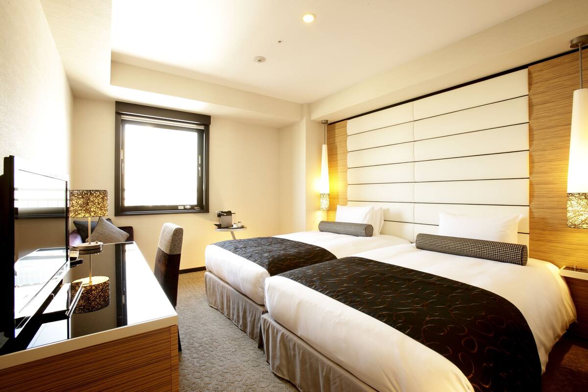 Une chambre d’hôtel avec deux lits, un bureau, une chaise, une télévision et une fenêtre.