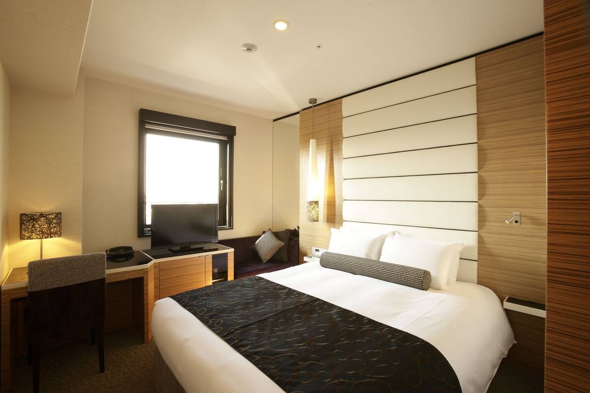 Une chambre d’hôtel équipée d’un lit, d’un bureau, d’une chaise, d’une télévision et d’une fenêtre.