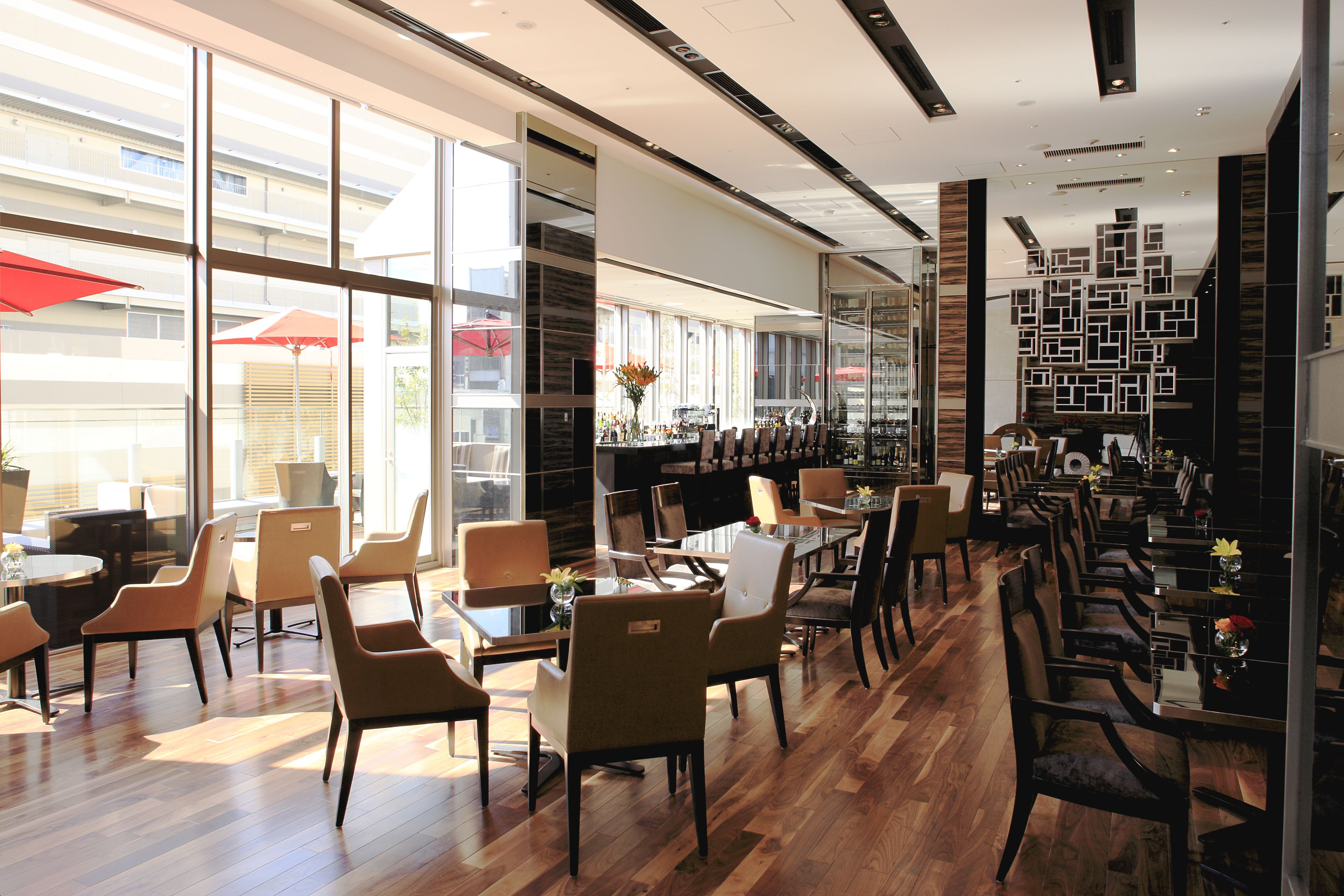 A modern restaurant with wooden flooring, glass partitions, and red umbrellas outside.