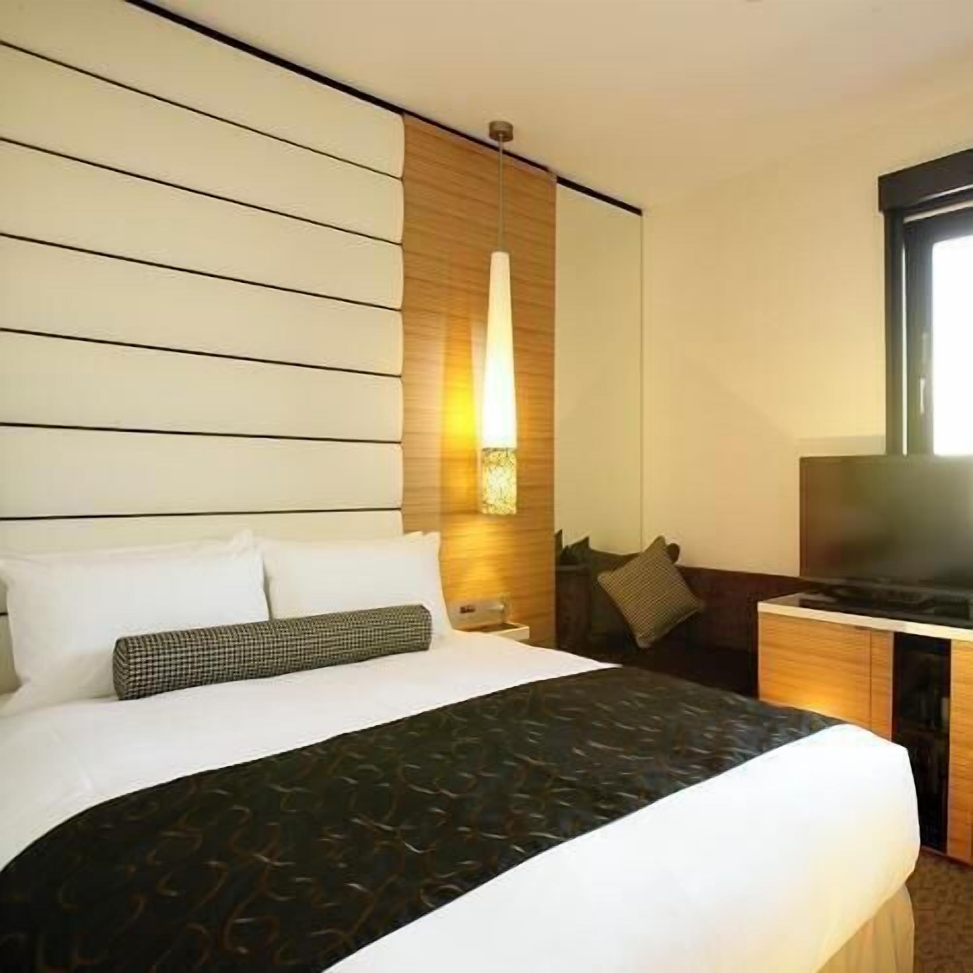 Une chambre d’hôtel avec un lit, une table de chevet, une lampe et un téléviseur.