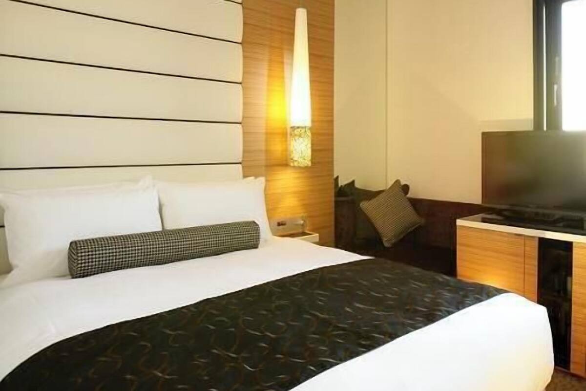 Une chambre d’hôtel avec un lit, une table de chevet, une lampe et un téléviseur.