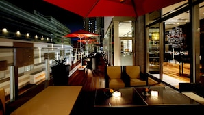 Een buitenterras met tafels, stoelen en rode parasols.