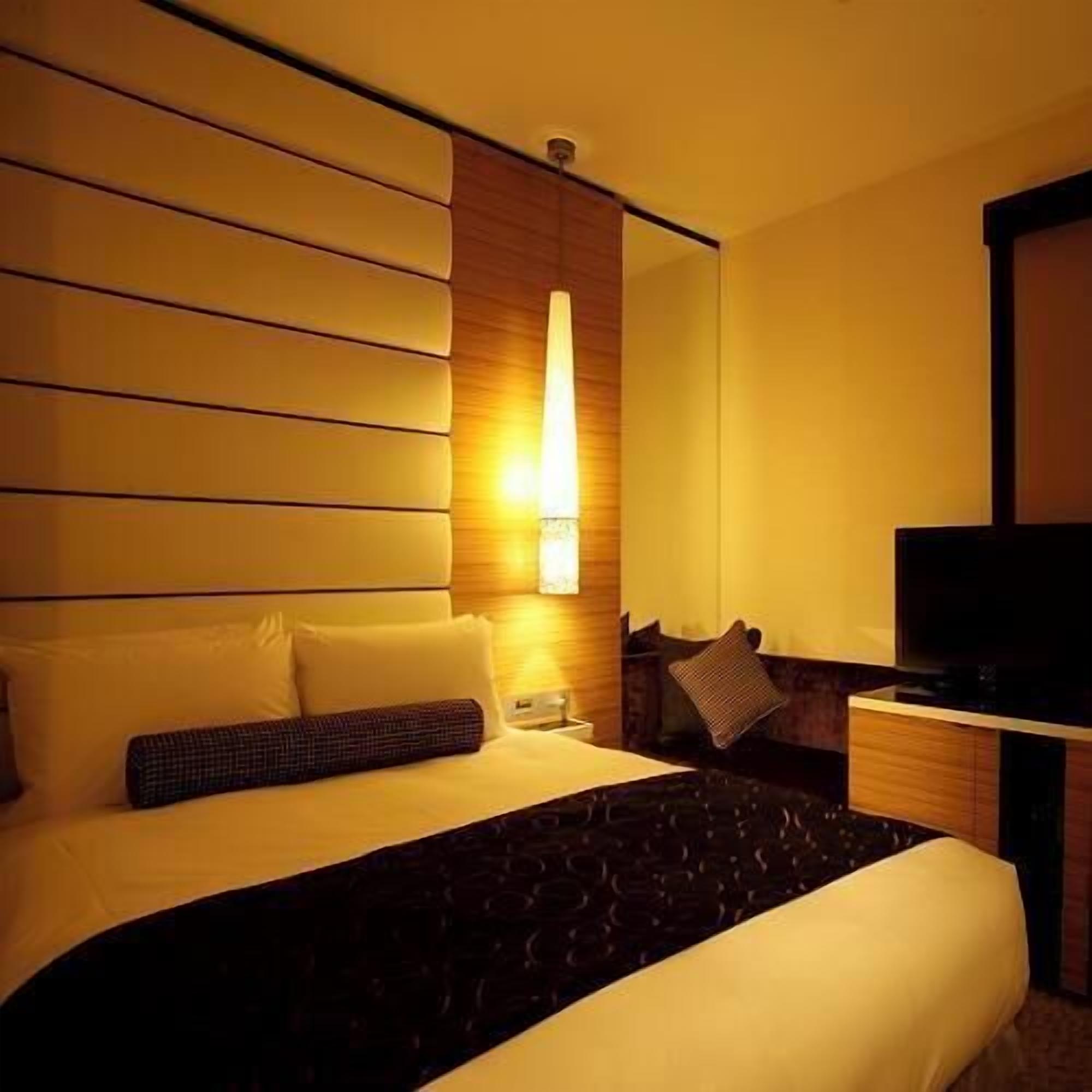 Une chambre d’hôtel équipée d’un lit, d’une télévision, d’un bureau et d’une lampe fixée au mur.