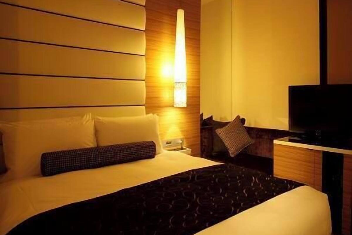 Une chambre d’hôtel équipée d’un lit, d’une télévision, d’un bureau et d’une lampe fixée au mur.