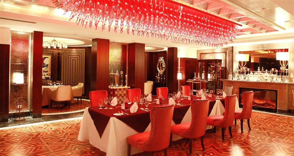 A formal dining area with red chairs and white tablecloths, a bar with a wine display, and a decorative ceiling.