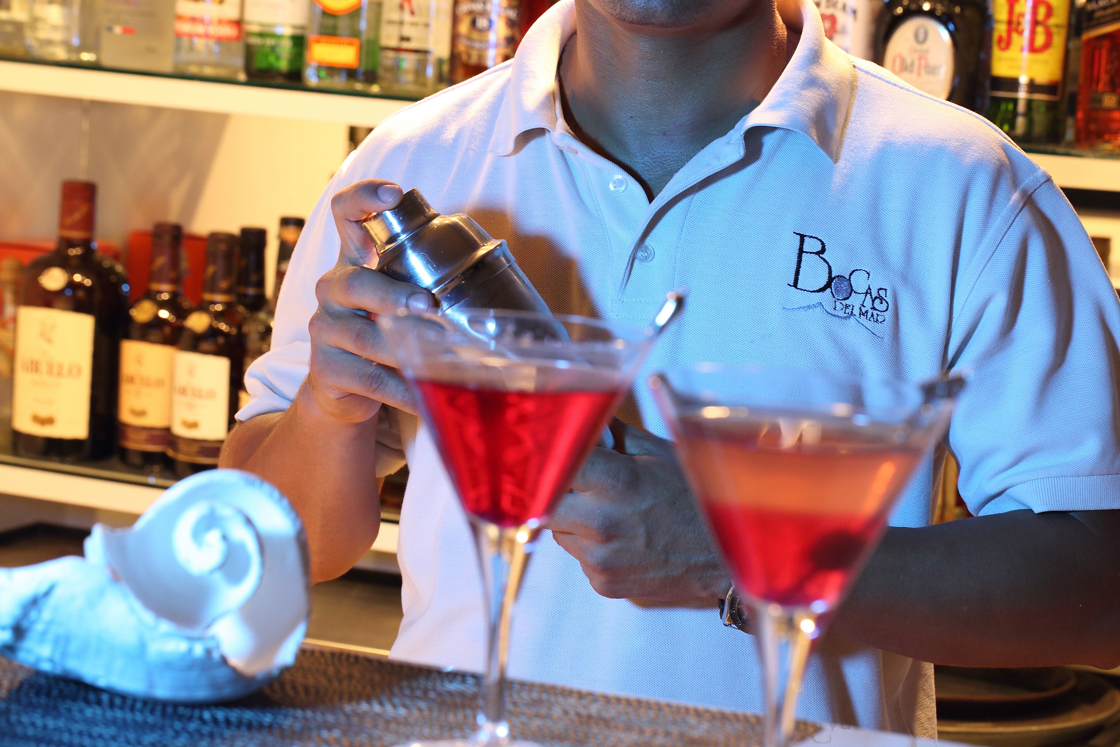 Un bartender preparando cócteles en un bar, con varias botellas al fondo.